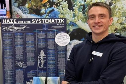Räuber in unseren Meeren - warum Haie unseren Schutz benötigen Zu sehen ist Felix Katzenberger stehend neben seinem Ausstellungstisch