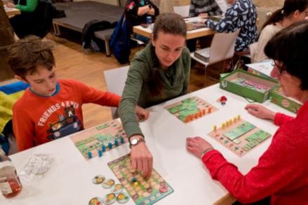 Spielertreff ein Junge und zwei Frauen die zusammen ein Brettspiel spielen.
