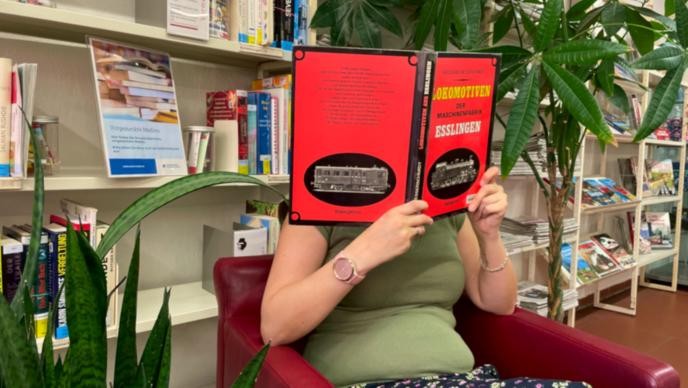 Vormerkung Person vor dem Vormerkungsregal mit Buch in der Hand