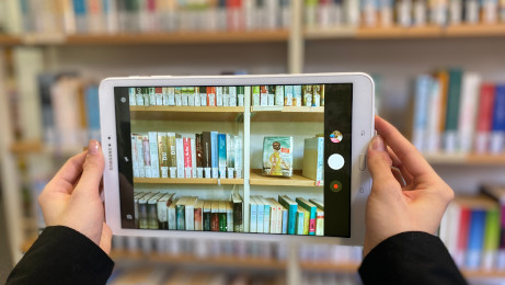 Tablet mit Foto von Büchern vor Bücherregal