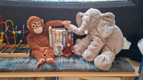 Kuscheltiere (Affe und Elefant) sitzen im Bücherbus, zwischen ihnen sind Bücher